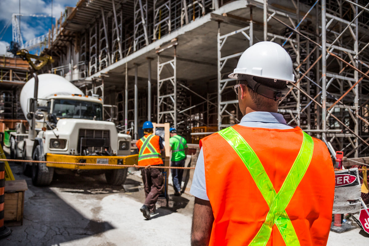 Construction worker wearing a white hard hat and orange reflective safety vest at an active jobsite